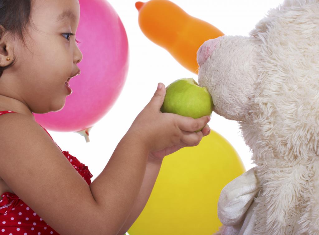 девочка кормит яблоком игрушечную собаку